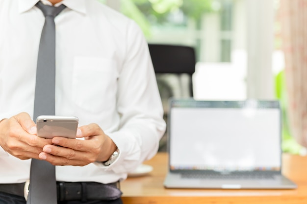 Businessmans hand met mobiele telefoon met laptop op houten bureau