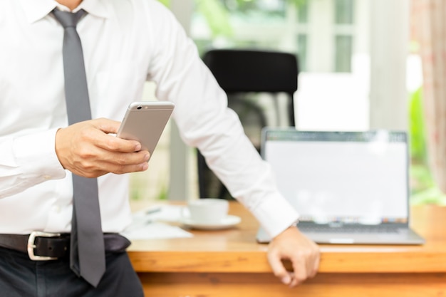 Businessmans hand met mobiele telefoon met laptop op houten bureau