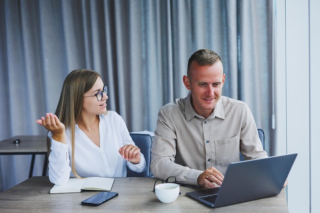 Businessmen are discussing while working with laptop in the office Focused business people cooperating in a modern workspace Two young businessmen are sitting together at a table