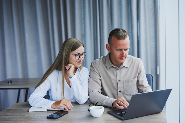 Businessmen are discussing while working with laptop in the office Focused business people cooperating in a modern workspace Two young businessmen are sitting together at a table