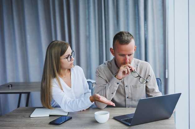 Businessmen are discussing while working with laptop in the office Focused business people cooperating in a modern workspace Two young businessmen are sitting together at a table