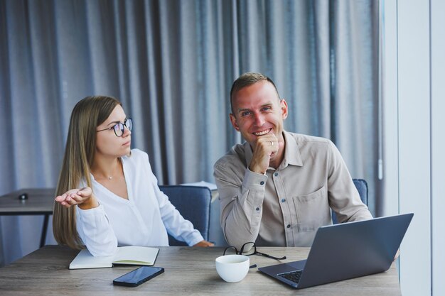 Businessmen are discussing while working with laptop in the office Focused business people cooperating in a modern workspace Two young businessmen are sitting together at a table