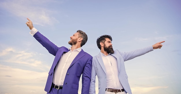 Businessmen bearded faces stand back to back sky background Men formal suit managers pointing at opposite directions Changing course New business directions Developing business direction