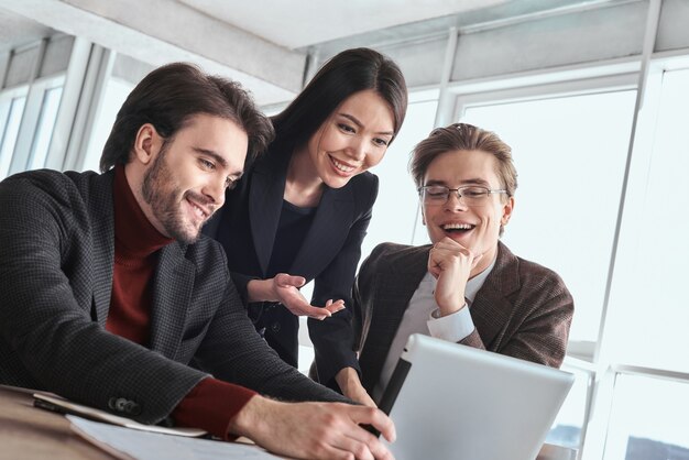 Uomini d'affari e donne d'affari in ufficio che lavorano insieme seduti al tavolo guardando video online su tablet digitale sorridenti gioiosi