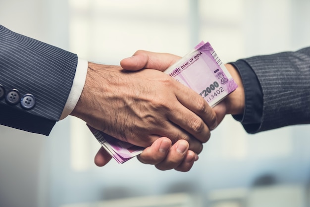 Businessmen making handshake with money, Indian Rupee currency, in hands