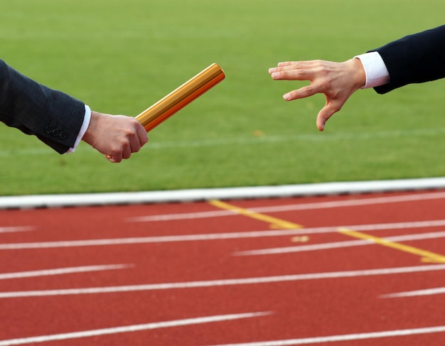 Photo businessmen pass on the baton in relay race in stadium