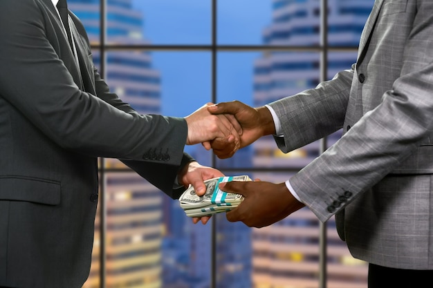 Businessmen&amp;#39;s handshake and money transfer. Financial deal beside skyscraper. Simple and effective approach. Be attentive with your partners.