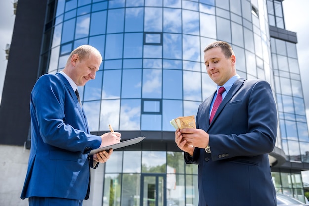 Businessmen signing contract with euro banknotes outdoors