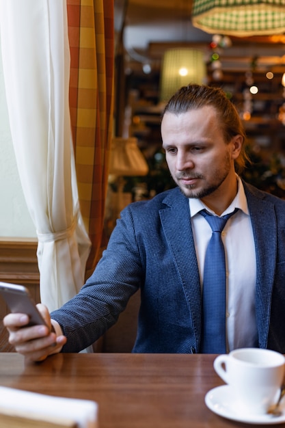 Businessmen sitting inside cafe bar reading a message on  the mobile phone during coffe break.