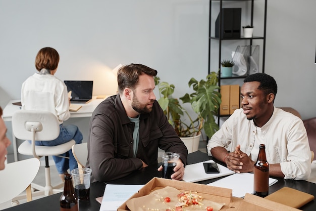 Businessmen sitting at office with drinks and food after work