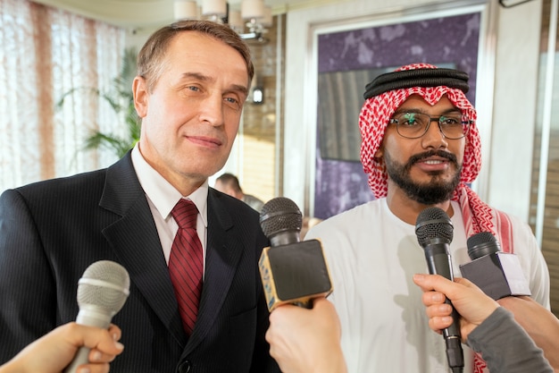 Businessmen standing in front of journalists with microphones during interview