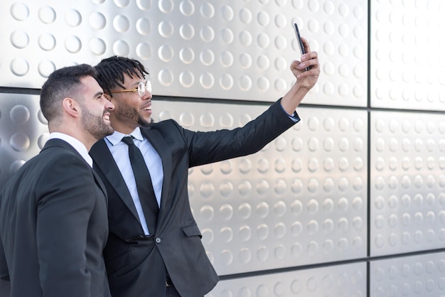 Uomini d'affari che prendono selfie al muro d'argento della strada