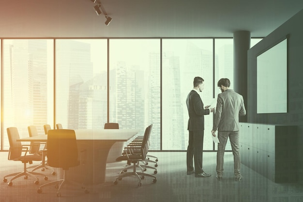 Businessmen talking in gray meeting room interior with panoramic window, long white table and black and white chairs. Mock up screen hanging above lockers. Toned image double exposure