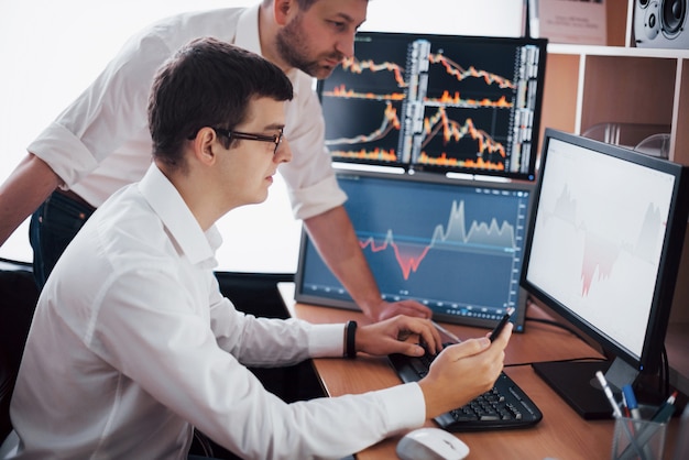 Businessmen trading stocks online. Stock brokers looking at graphs, indexes and numbers on multiple computer screens. Colleagues in discussion in traders office. Business success concept.