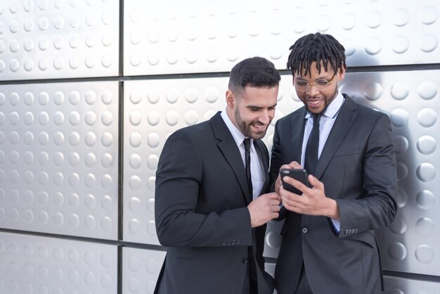 Businessmen using smartphone at street silver wall