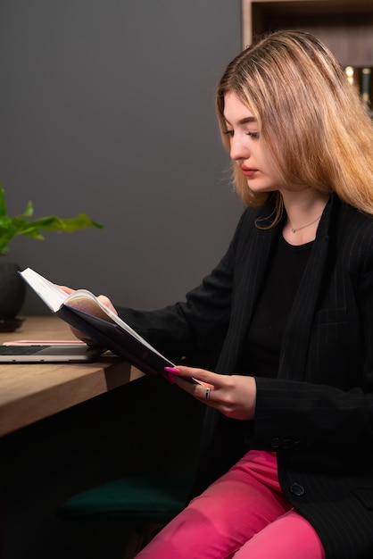 Businessowman zit een boek of tijdschrift te lezen aan haar bureau op kantoor terwijl ze haar agenda bestudeert of marktonderzoek doet in een close-up bijgesneden weergave