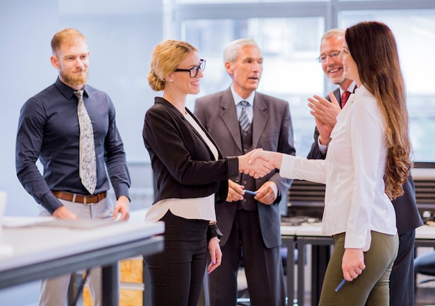 Businesspeople applauding two smiling businesswoman shaking hands