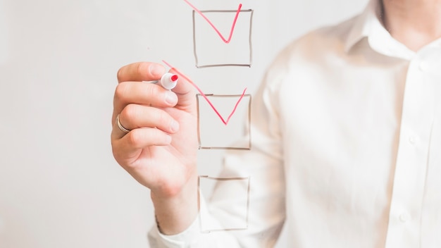 Businessperson's hand ticking off check boxes with red marker on screen