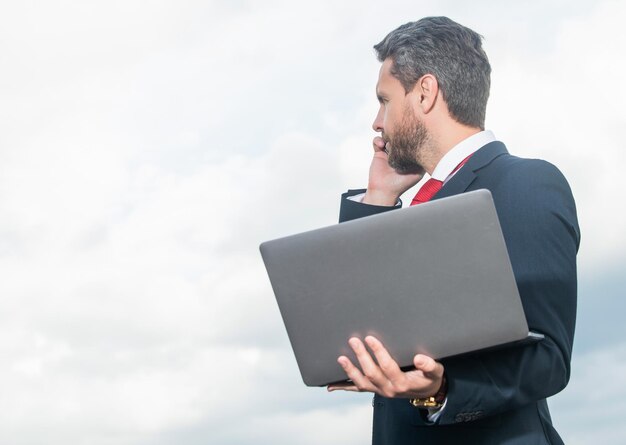 Businessperson in suit speaking on phone and hold laptop