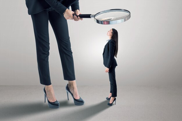 Photo businessperson in suit using magnifier magnifying glass to look at tiny female subordinate on concrete background with shadow and mock up place hiring and dominance concept