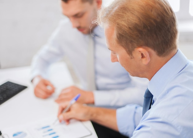 businesss and office concept - businessmen with notebook discussing graphs on meeting