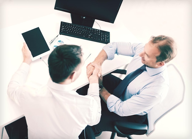 businesss and office concept - two businessmen shaking hands in office