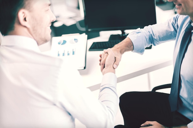 businesss and office concept - two businessmen shaking hands in office