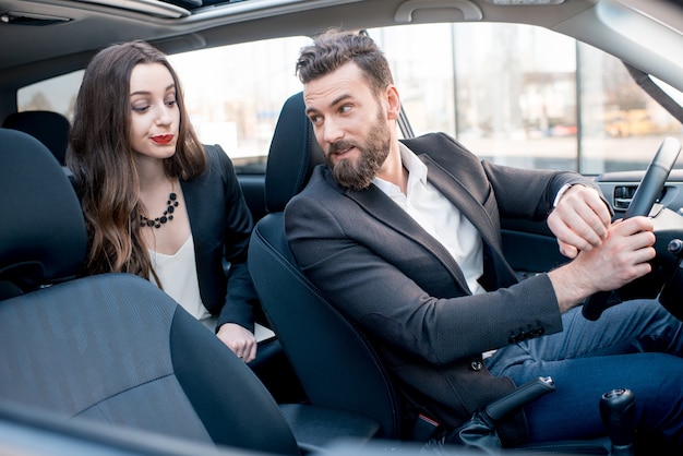 Imprenditrice sul sedile posteriore con un uomo elegante alla guida di un'auto in città. preoccupato per un ritardo in un incontro importante