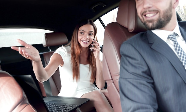 Businesswoman on the backseat with elegant man driving a car in the city