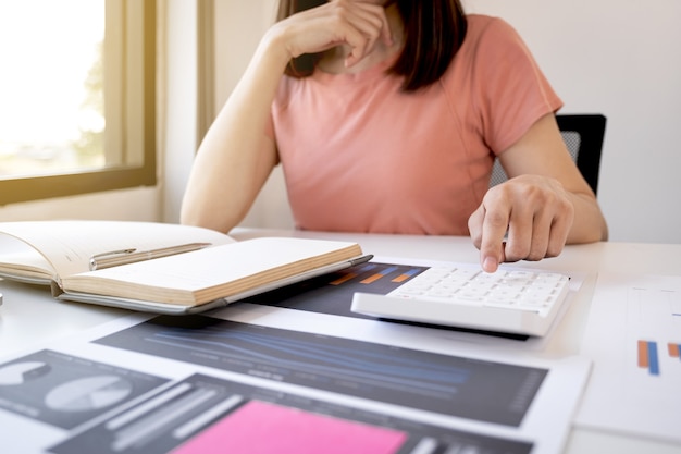 Calcolatrice di uso della mano del contabile della donna di affari e analisi del grafico con il computer portatile all'ufficio domestico