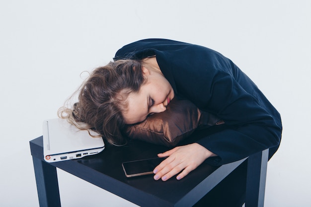 Businesswoman in a business suit and with phone and laptop sleeping on a table