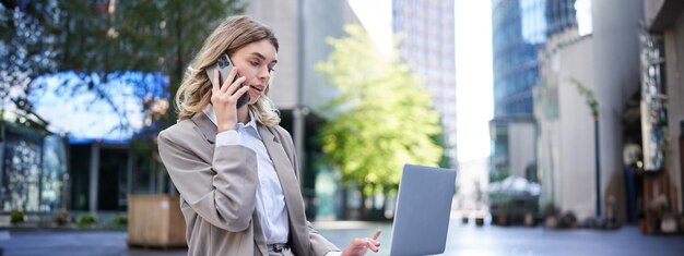 Photo businesswoman checking diagram and work on laptop calling someone on mobile phone sitting outdoors