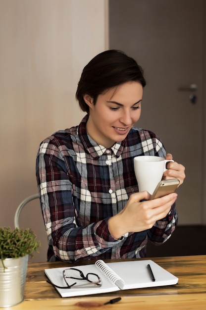 A businesswoman checking email via mobile phone and holding a coffee cup at home