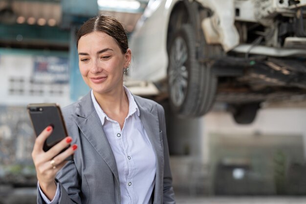 Businesswoman client using smartphone talking with agent claim insurance her car at garage service