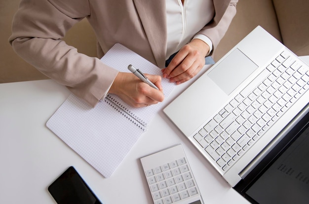 businesswoman counts the budget and makes notes in a notebook on the desktop with a calculator