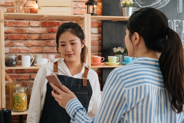 스마트폰과 nfs 첨단 기술을 사용하여 아침 카페 바에서 바리스타에게 구매 비용을 지불하는 사업가 고객. 휴대폰 거래 및 온라인 결제. 클라이언트가 웨이트리스에게 휴대폰을 보여줍니다.