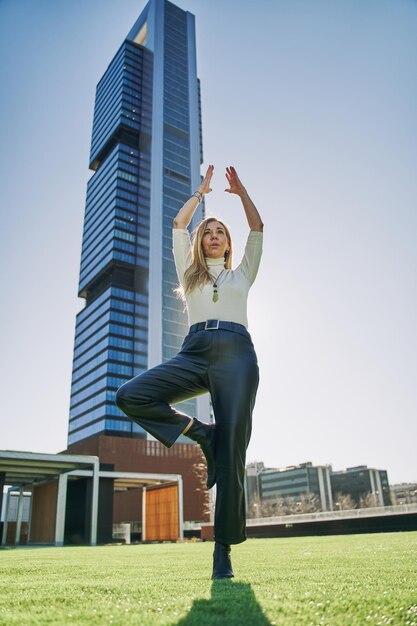 A businesswoman doing yoga during a break from office work with an office building in the background