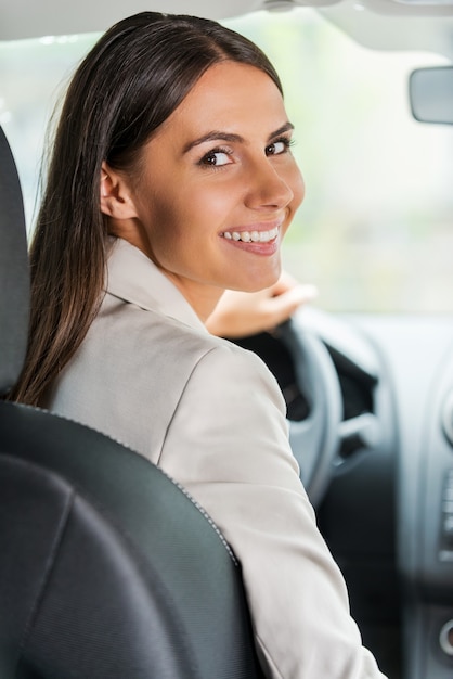 実業家の運転車。車を運転し、肩越しに見ている自信を持って若い実業家の背面図