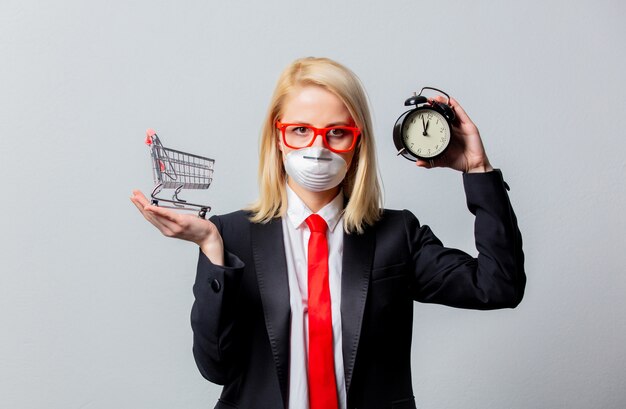 Businesswoman in face mask and red glasses holds alarm clock and cart