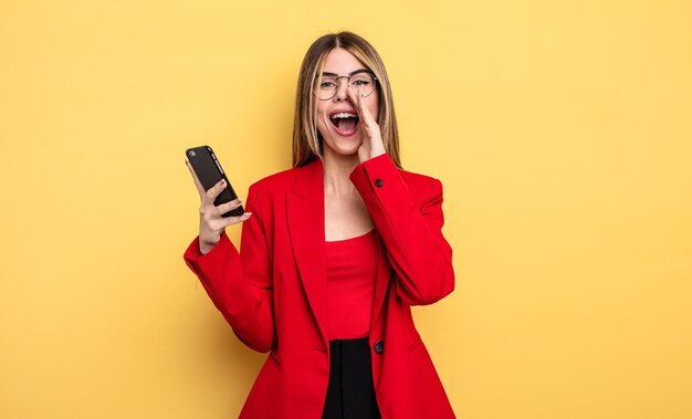 Photo businesswoman feeling happy,giving a big shout out with hands next to mouth. smartphone concept