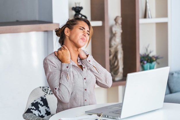 Businesswoman feeling pain in neck after sitting at the table with laptop.