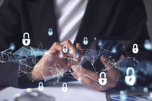 A businesswoman in formal wear checking the phone to sign the\
contract to prevent probability of risks in cyber security padlock\
hologram icons over the working desk