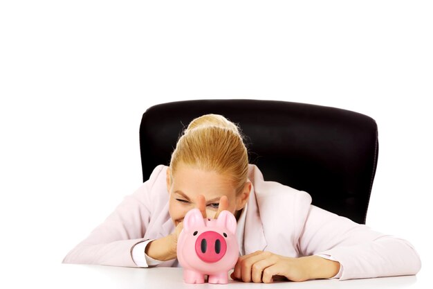 Businesswoman gesturing peace sign by piggy bank against white background