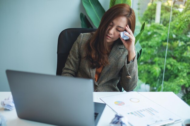 実業家は、オフィスでの仕事で問題を抱えている間、テーブルの上のめちゃくちゃな紙とラップトップでストレスを感じる