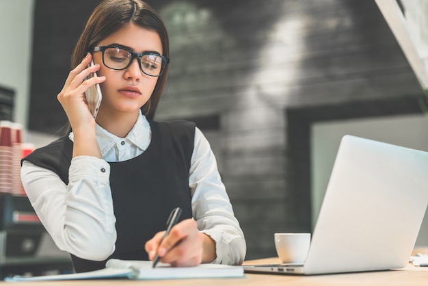 The businesswoman in glasses phones at the desktop