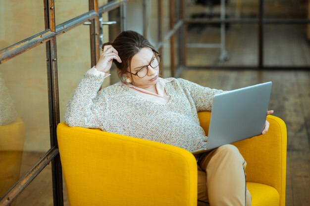 Foto imprenditrice con gli occhiali. donna d'affari incinta che indossa un maglione elegante e occhiali mentre si lavora sul laptop