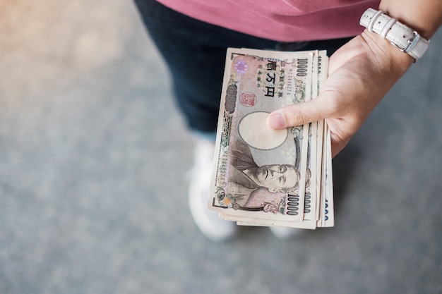 Рука коммерсантки держа стог банкноты японских иен. концепции бизнеса, денег, инвестиций, финансов и платежей