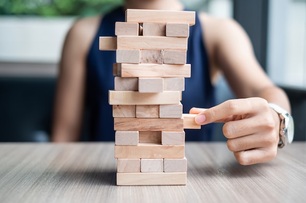 Businesswoman hand placing or pulling wooden block on the tower