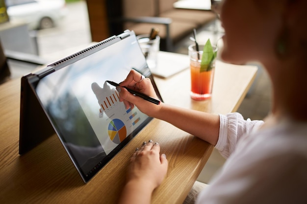 Foto donna d'affari con la mano che indica con lo stilo sul grafico sullo schermo del portatile convertibile in modalità tenda donna che utilizza un notebook 2 in 1 con touchscreen per il lavoro sulla presentazione aziendale vista ravvicinata isolata