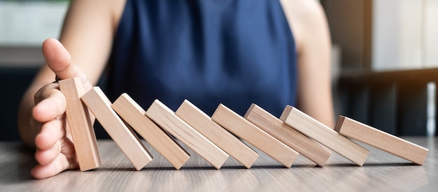 Businesswoman hand Stopping Falling wooden Dominoes